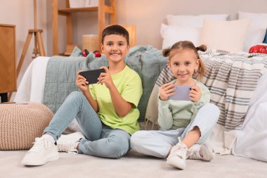 Cep telefonlu şirin çocuklar evde yerde video oyunu oynuyorlar.