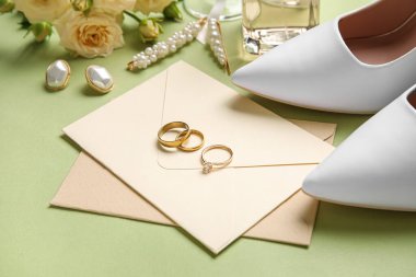 Nişan yüzükleri, zarflar ve yeşil arka planda gelinlik aksesuarları.