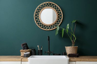 Banyoda yeşil duvarın yanında banyo aksesuarları ve bitkiler var.