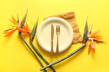 Sarı arka planda güzel strelitzia çiçekleri, çatal bıçak takımı ve peçeteli bir tabak.