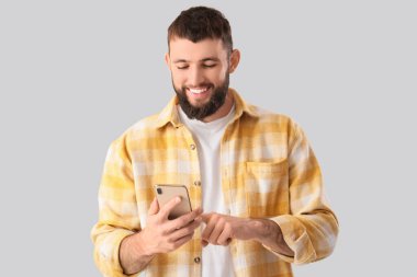 Gri arka planda cep telefonu olan yakışıklı genç adam.