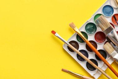 Sanatçı sarı arka planda fırçalar ve boyalar