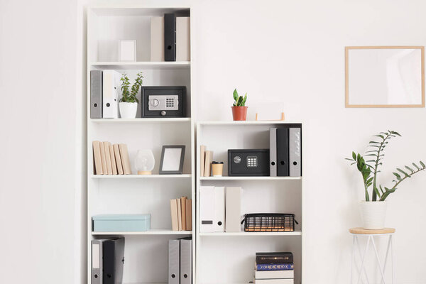 Modern safes, houseplants and office folders on shelving unit near white wall