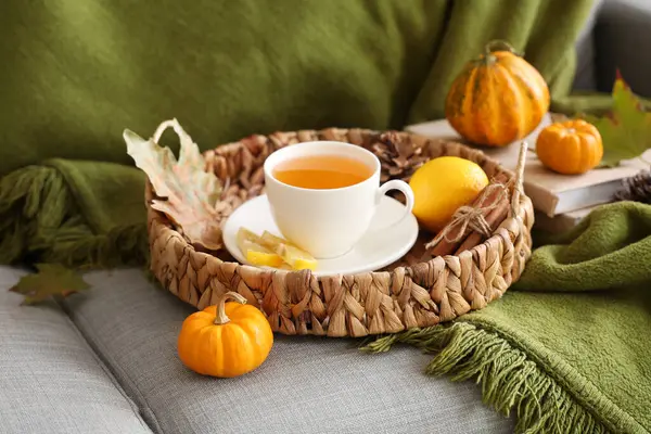 Ekose, hasır tepsi, çay demliği, bir fincan sıcak yeşil çay, balkabağı ve sonbahar yaprakları odadaki kanepede.