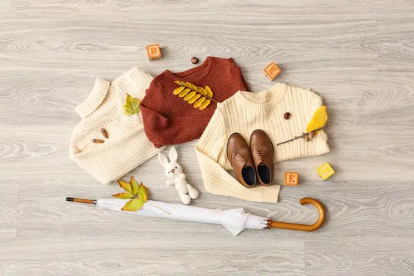 Hafif ahşap zemin üzerinde şık çocuk kıyafetleri, oyuncaklar, şemsiye ve sonbahar yaprakları olan kompozisyon