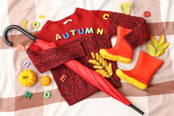 Şık çocuk süveteri, lastik botları, şemsiyesi ve açık kumaş arka planda düşmüş yaprakları olan kompozisyon