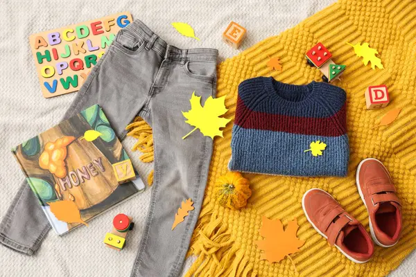 Şık çocuk kıyafetleri, oyuncakları, ekoseli ve kâğıtlı kompozisyon açık kumaş arka planında sonbahar yaprakları