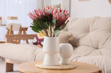 Oturma odasındaki sehpanın üzerinde güzel protea çiçekleri olan vazo.