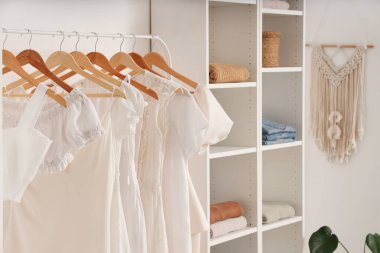 Aydınlık duvarın yanında farklı kadın kıyafetleri olan raflar.