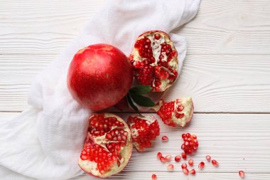 Tohumlarla taze nar ve beyaz ahşap arka planda yapraklar.