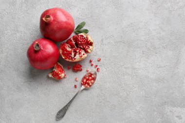 Taze olgun nar ve kaşık, gri arka planda tohumlar.