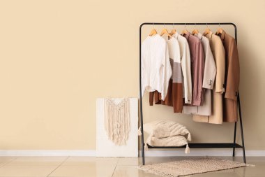 Farklı şık kıyafetler ve bej duvarın yanında yumuşak yastıklar.