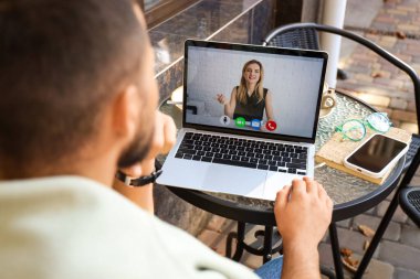 Dizüstü bilgisayarlı genç adam sokak kafesindeki masada sohbet ediyor, yakın plan.