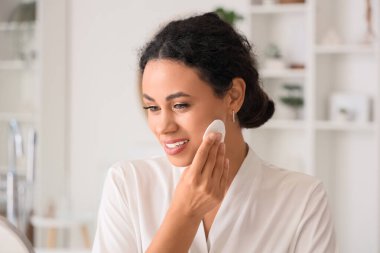 Güzel bir Afro-Amerikalı kadın banyoda pamukla makyaj yapıyor.