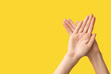 Sarı arka planda kalp hareketi gösteren kadın eller.