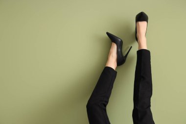 Yeşil arka planda topuklu siyah pantolonlu kadın bacakları.