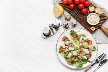 Lezzetli tavuklu Sezar salatası ve beyaz arka planda malzemeler.