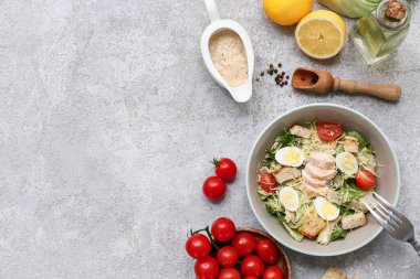Lezzetli tavuklu Sezar salatası ve gri arka planda malzemeler.