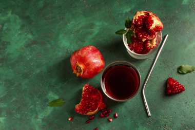 Bir bardak taze nar suyu ve yeşil arka planda meyveler.