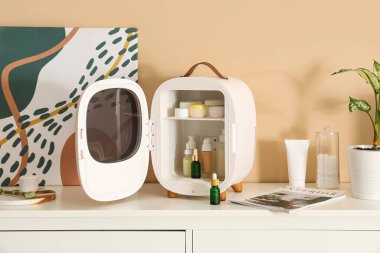 Bej duvarın yanındaki çekmecelerde kozmetik ürünleri olan küçük bir buzdolabı aç. Yakın çekim.