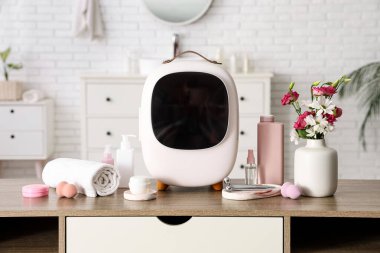 Cilt ürünleri, havlu ve vazodaki çiçeklerle kaplı kapalı kozmetik buzdolabı beyaz duvarın yanındaki masada. Yakın çekim.