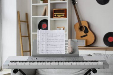 Oturma odasında nota kağıtları ve kulaklıkları olan modern sentezleyici