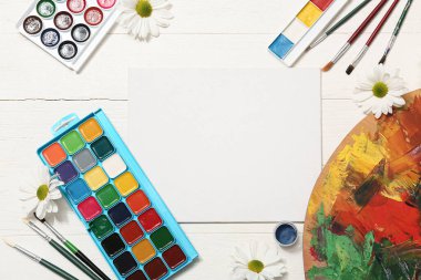 Sanatçı fırçaları, boyalar, boş tuval ve beyaz ahşap arka planda çiçekler