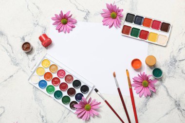 Beyaz mermer zemin üzerinde sanatçı fırçaları, boyalar ve çiçekler olan bir sayfa kağıt.