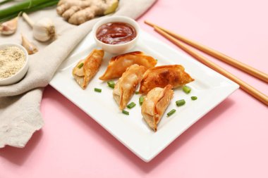 Pembe arka planda yeşil soğanlı ve bir kase soslu kızarmış Japon gyozası.