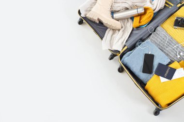 Kış aksesuarlarıyla bavulu aç ve arka planda cep telefonu, üst görünüm