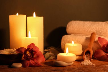 Koyu ahşap masada yanan mumlar ve orkide çiçekleri olan spa kompozisyonu