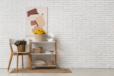 Kasımpatı çiçekli sepetler ve beyaz tuğla duvara karşı sandalyenin yanındaki raf ünitesinde ev dekoru.