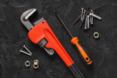 Vidalar, vidalar, boru anahtarı ve siyah grunge arka planda tornavida.