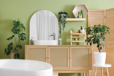 Lavabosu, aynası ve yeşil bitkileri olan bir banyo.