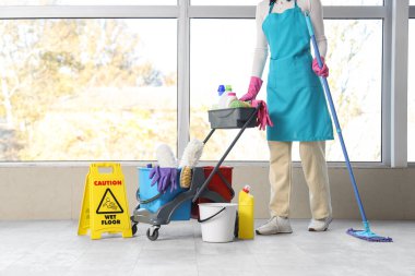 Oda penceresinin yanında temizlik malzemeleriyle dolu tramvayı olan kadın hademe.