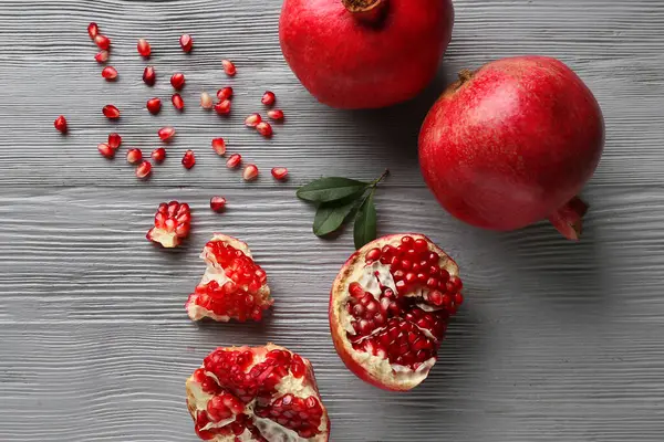 Gri ahşap arka planda tohum ve yapraklarla taze olgun narlar.