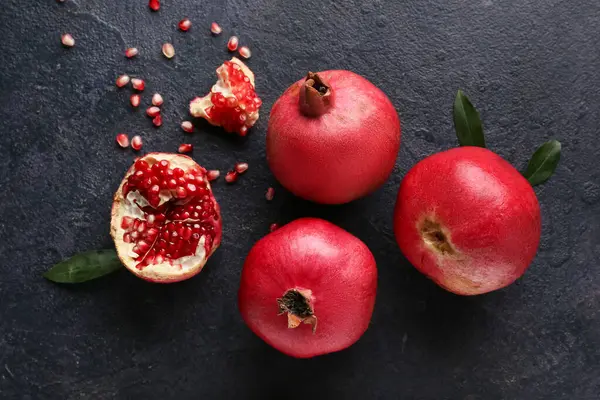 Koyu arkaplanda tohum ve yapraklarla taze olgun nar.