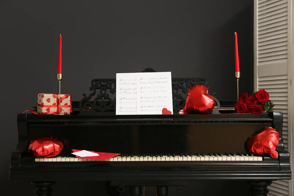 Piano with note sheets and decor for Valentine's Day near dark wall in room