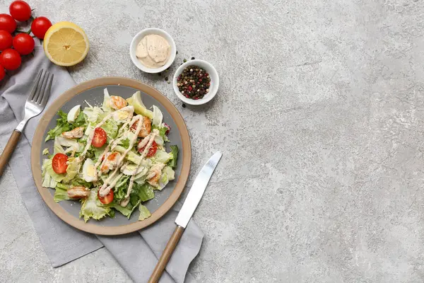 Lezzetli tavuklu Sezar salatası, limon, bir kase sos ve gri arka planda biberli mısır.