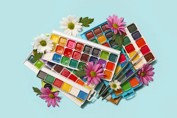 Mavi arka planda sanatçı fırçaları, boyalar ve çiçekler