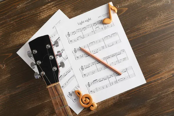 Müzik kağıtları, nota işaretleri, tahta arka planda kalem ve gitar.