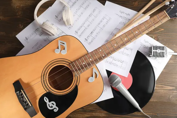 Gitar, mikrofon, nota kağıtları ve ahşap arka planda kulaklıkla kompozisyon