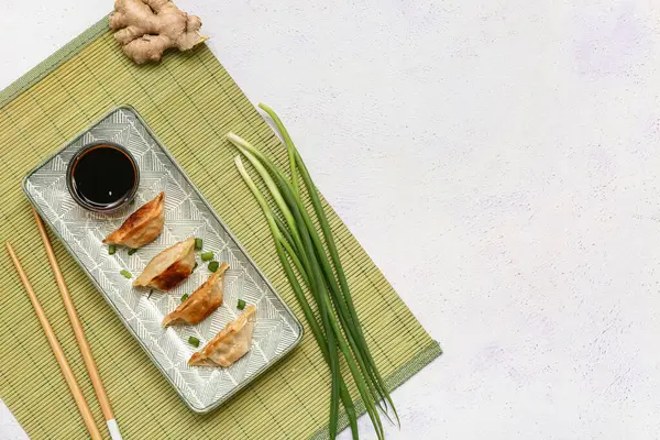 Yeşil soğanlı kızarmış Japon gyozası ve beyaz arka planda bir kase soya sosu.