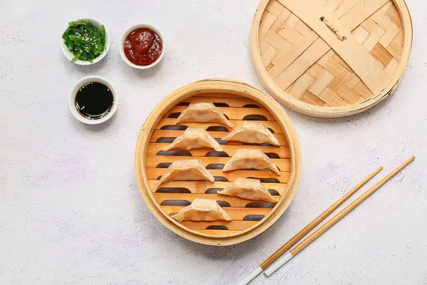 Lezzetli Japon gyozası ve beyaz arka planda soslu bambu tenceresi.