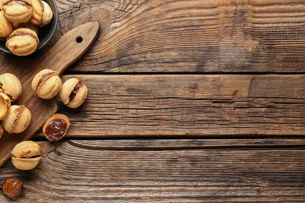 Tahta zemin üzerinde kaynamış konsantre süt ve ceviz şeklinde kurabiyeler kâse ve kesme tahtası.