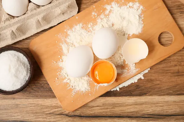 Tahta arka planda hamur hazırlamak için yumurta, un ve bir kase tuz.