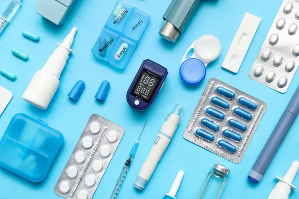 Nabız oksimetresi, konteynır kontak lensler, termometre ve mavi arka planda ilaçlar.