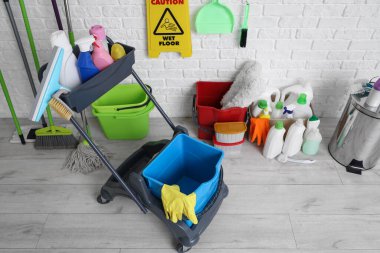 Beyaz tuğla duvarın yanında bir sürü temizlik malzemesi ve uyarı levhası olan bir araba.