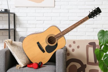 Modern akustik gitar, gri koltukta kulaklıklar şık oturma odasında.