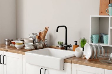 Seramik lavabo, temiz tabaklar ve mutfak aletleri ahşap tezgahta.